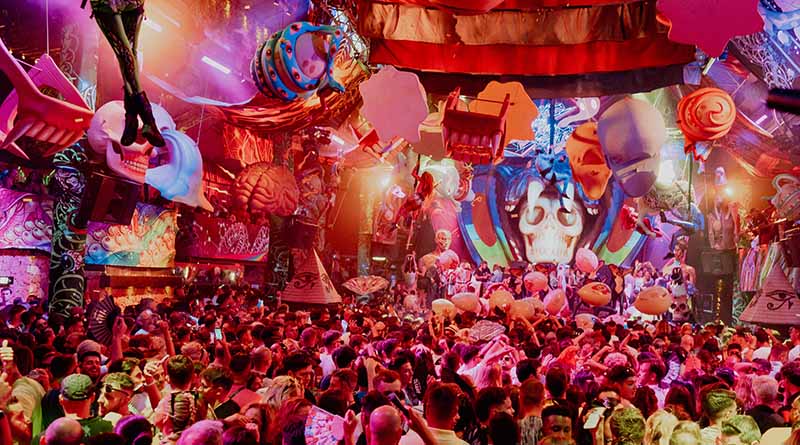 Escenario de elrow decorado con motivos coloridos de la Noche de los Muertos, con el público bailando durante una sesión de música electrónica