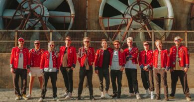 Los once integrantes de MEUTE posan con sus característicos uniformes rojos de músico de banda